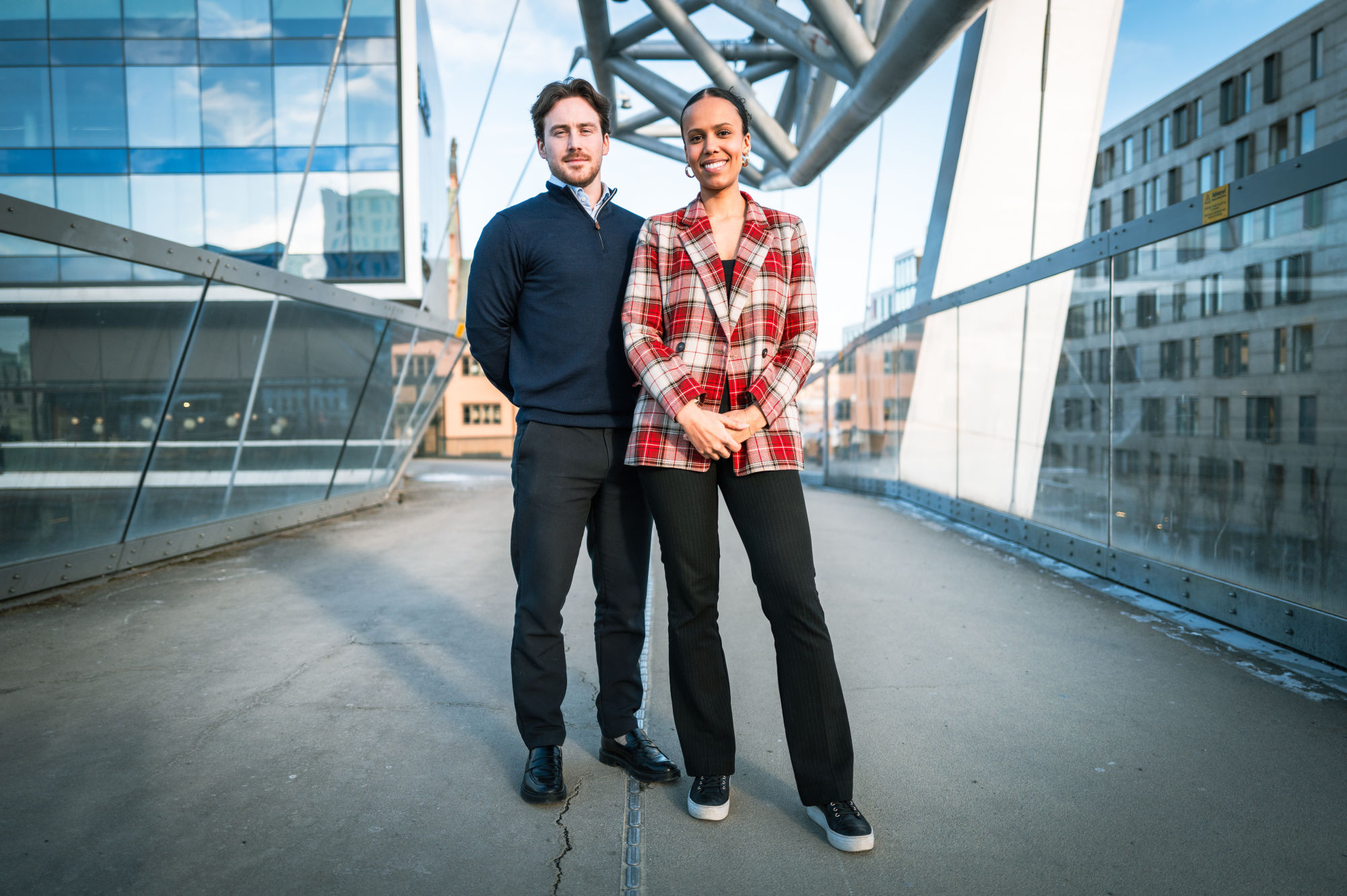 David og Amanda står på en gangbro i glass og metall utenfor kontoret i Oslo.