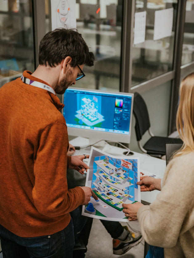 Faglærer og student ser på et spilldesign som er printet ut på papir. 