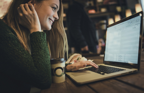 Kvinne som sitter foran en PC på kafe