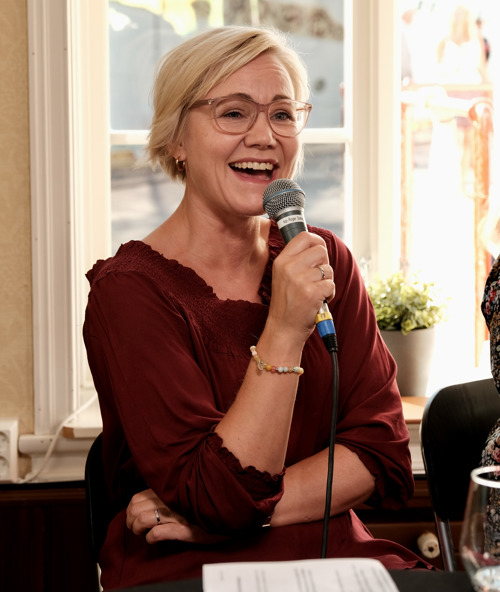 Ingvild Kjerkol fotografert under debatten. Hun sitter, har på seg en rød kjole og smiler mens hun holder en mikrofon.