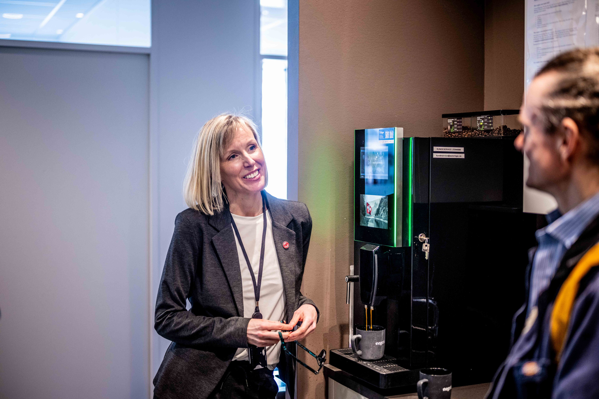 Kristine står ved kaffeautomaten son snakker med en kollega.