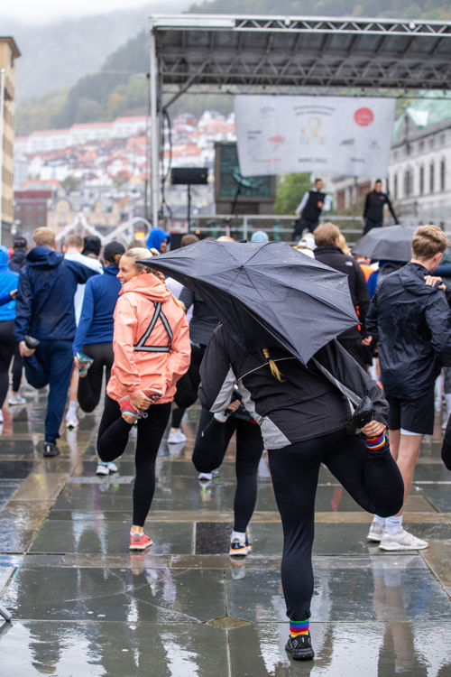 Mennesker står i regnvær på Torgallmenningen og tøyer ut til instruksjoner fra en scene.