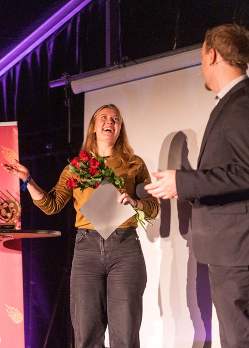 Foto av Sophia Aronsen som mottar pris og blomster på scenen.