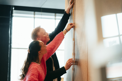 To studenter i interiørarkitektur måler med meterstokk på en vegg.