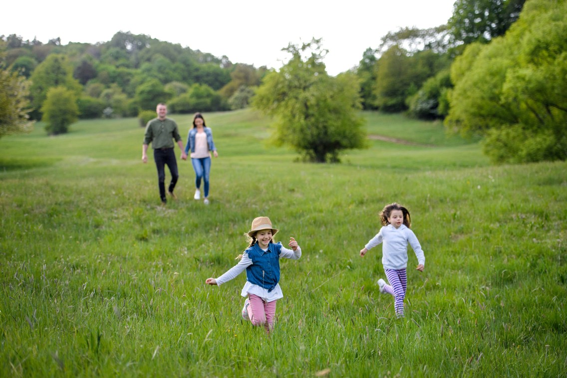 To voksne og to barn som går og løper på eng