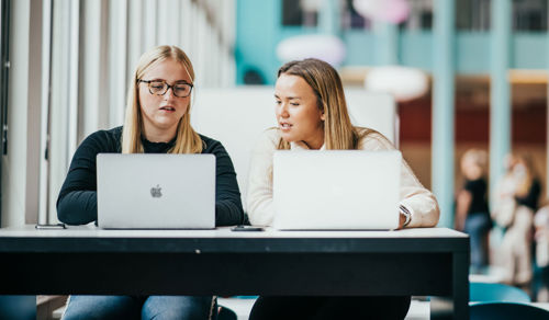 Foto av to jenter som sitter med hver sin mac på campus Bergen