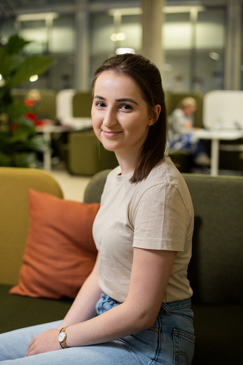 Emilie Hestnes er nettstudent i Kontormedarbeider på Fagskolen Kristiania. Hun sitter i en grønn sofa på Spikersuppa med faglærer. Hun har brunt, halvlangt hår og beige t-skjorte. 