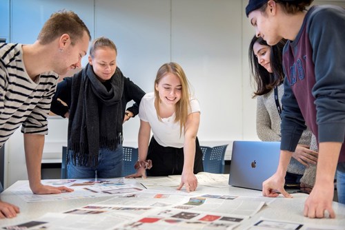 Fem studenter står samlet rundt et bord med utskrevede artikler. De diskuterer.