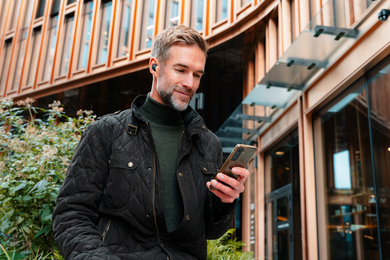 Mann ser på mobiltelefon, mens han står utenfor moderne kontorbygg.