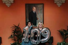 Administrerende direktør Solfrid Lind og rektor Trine Johansen Meza står foran portrettet av Ernst G. Mortensen, med oppblåste tall i hendene som til sammen viser 109. 