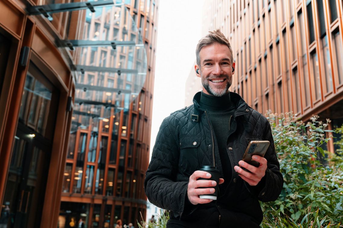 Man med mobiltelefon smiler til kamera.