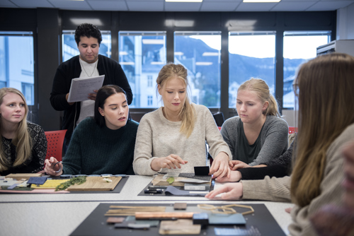 Foto av studenter som sitter samlet rundt et bord med interiørmodeller.