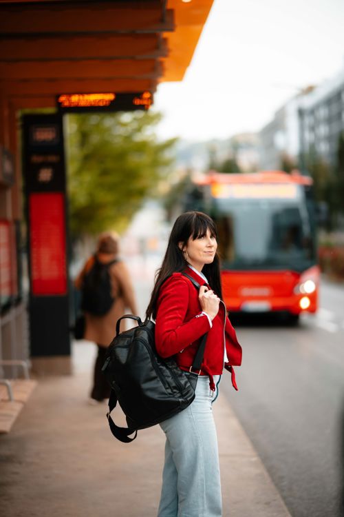 Kvinne med rød jakke venter på bussen