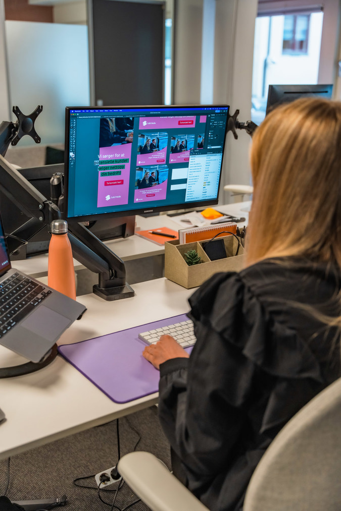 En person sitter ved en kontorpult med en dataskjerm