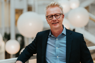 Foto av voksen mann med briller i blå skjorte og sort dressjakke.