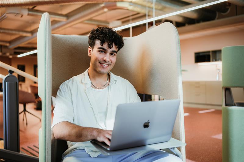 Ung mann sitter med mac i fanget.