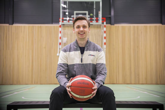 Gutt sitter å smiler med en basketball i hendene