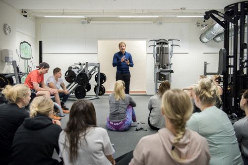 John Magne Kalhovde står i treningsrommet og snakker med studenter som sitter foran han og hører på.