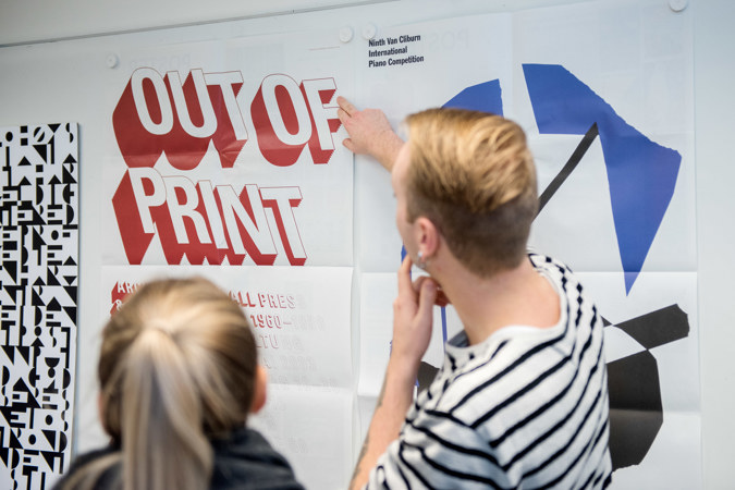 To personer studerer plakater som henger på en vegg