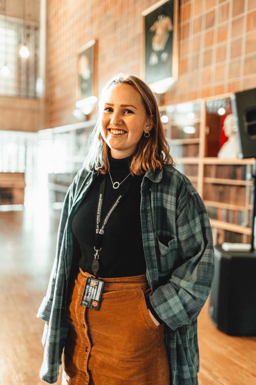 Bilde av ung kvinne i flanellskjorte som står i et bibliotek.