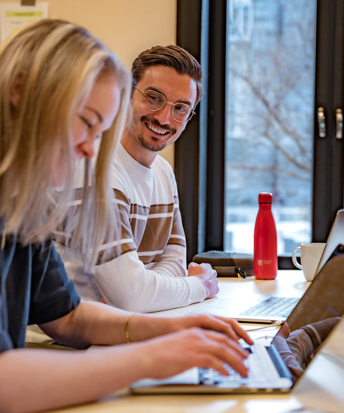 Foto av Caroline Klakegg og Øystein Thorheim som sitter ved siden av hverandre ved et bord. Caroline skriver på en Mac. 