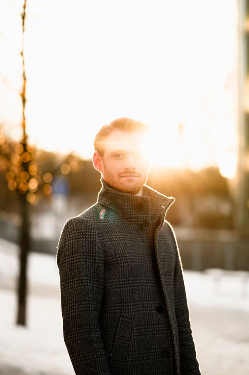 Ung mann i frakk utendørs med sol i bakgrunnen 