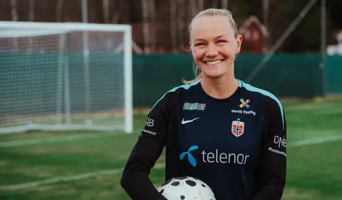 Frida står på banen og smiler mens hun holder en fotball.