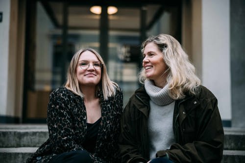 Adeline og Christin sitter på en steintrapp utendørs.