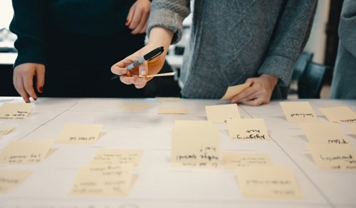 Foto av et bord fylt med post-it lapper. To personer står bak og sorterer.