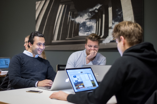 Bilde av unge mannlige studenter som sitter på et bord med hver sin laptop.