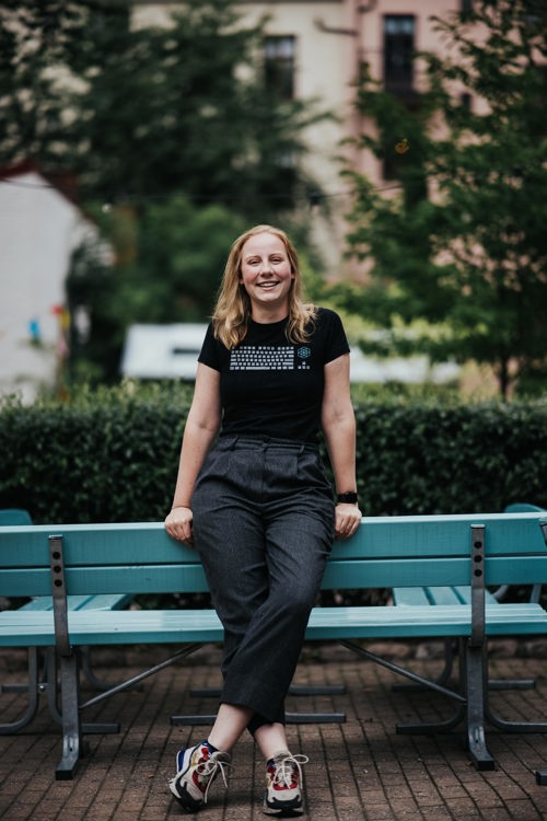 Blond kvinne i sort tøy lener seg på blå parkbenk.