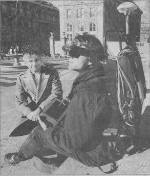 Old cut out from a newspaper showing a man sitting on a street corner with some technical device.