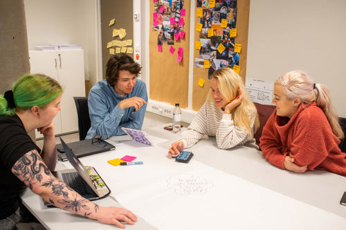 Foto av fire studenter ved et bord som snakker sammen.