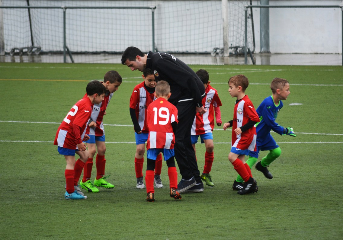 Småbarn som spiller fotball med en trener i midten