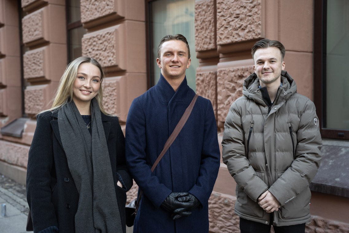 En gruppe på tre studenter som står i gaten utenfor campus. 