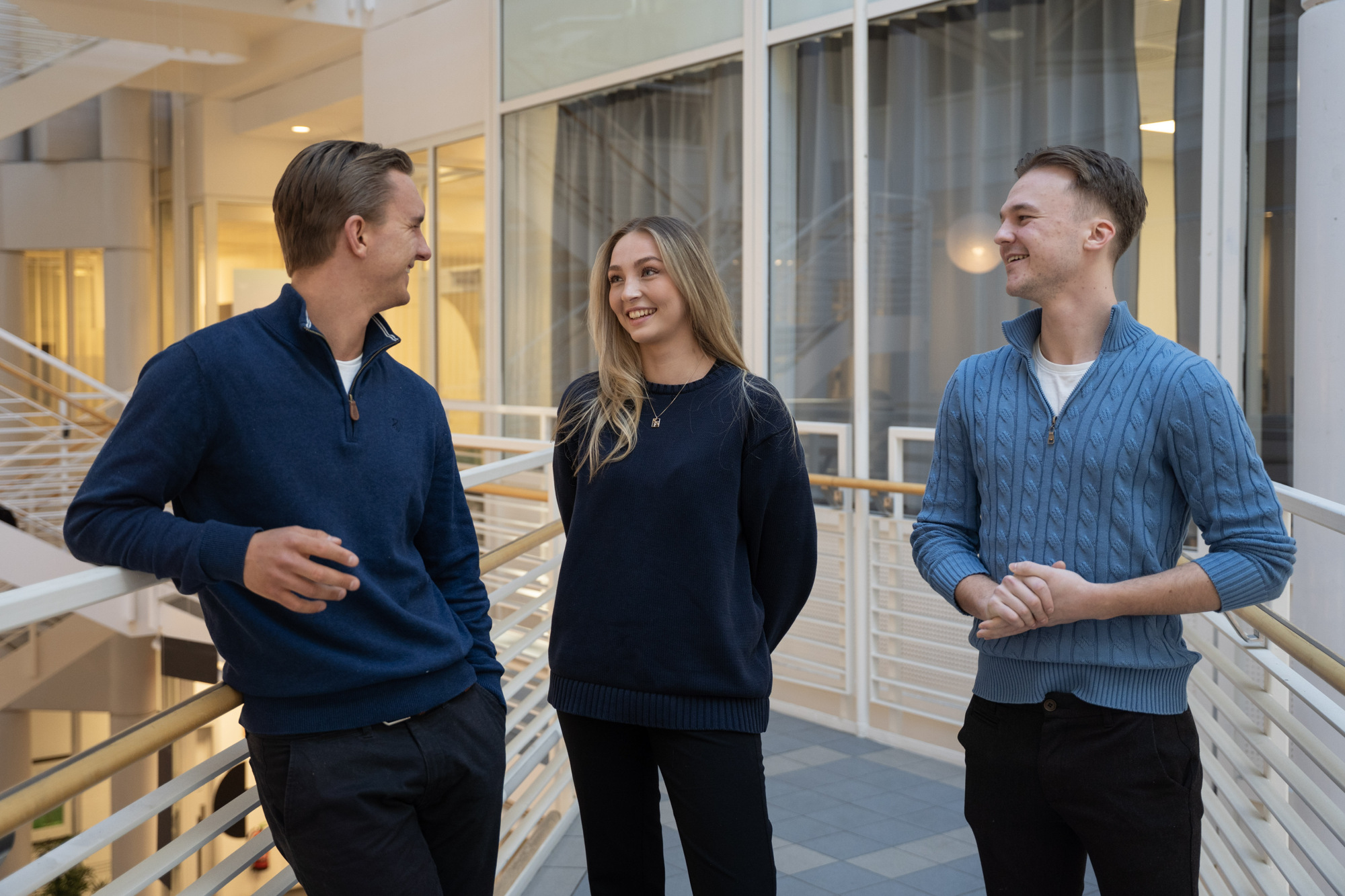 En gruppe på tre studenter som står og prater sammen inne på campus. 