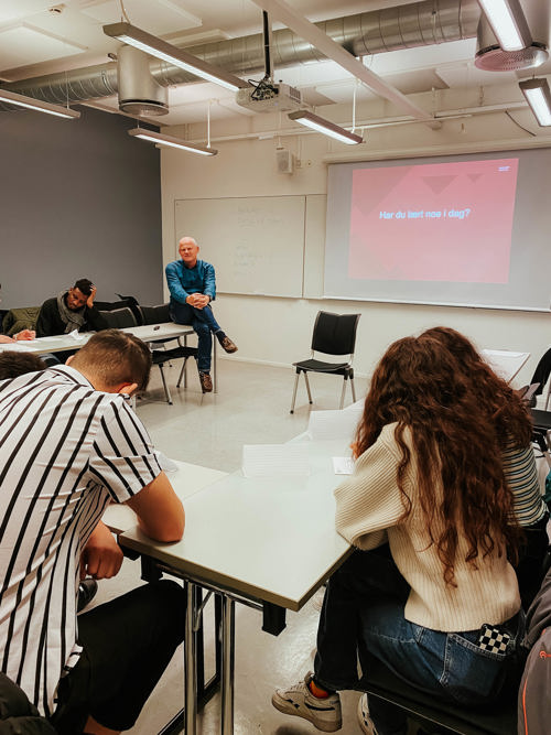  Studentene sitter med bøyde nakker over skrivepulter i en firkantformasjon vendt mot professor Nils Høgevold som foreleser til forsamlingen. Foto.