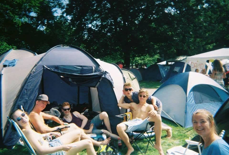 Ungdomsgjeng sitter i sommersola foran mange telt