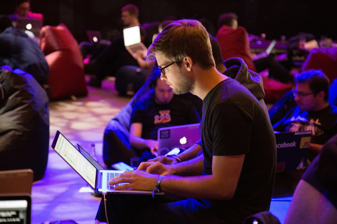 Young man with laptop, surrounded by more people on computers