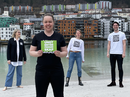 Foto av tre kvinner og en mann, på en strand. Bak dem ligger bydelen Gyldenpris i Bergen.