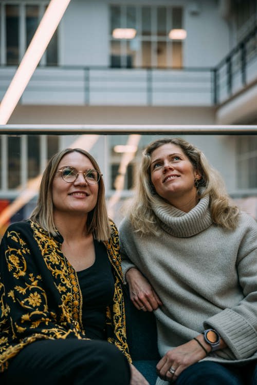 Adeline og Christin sitter i en trapp i et atrium.