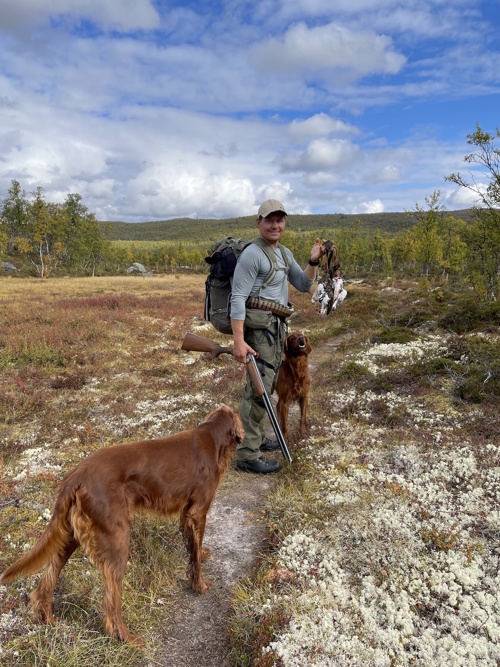 John Magne Kalhovde holder opp flere ryper. Han står på fjellet med sine to jakthunder.