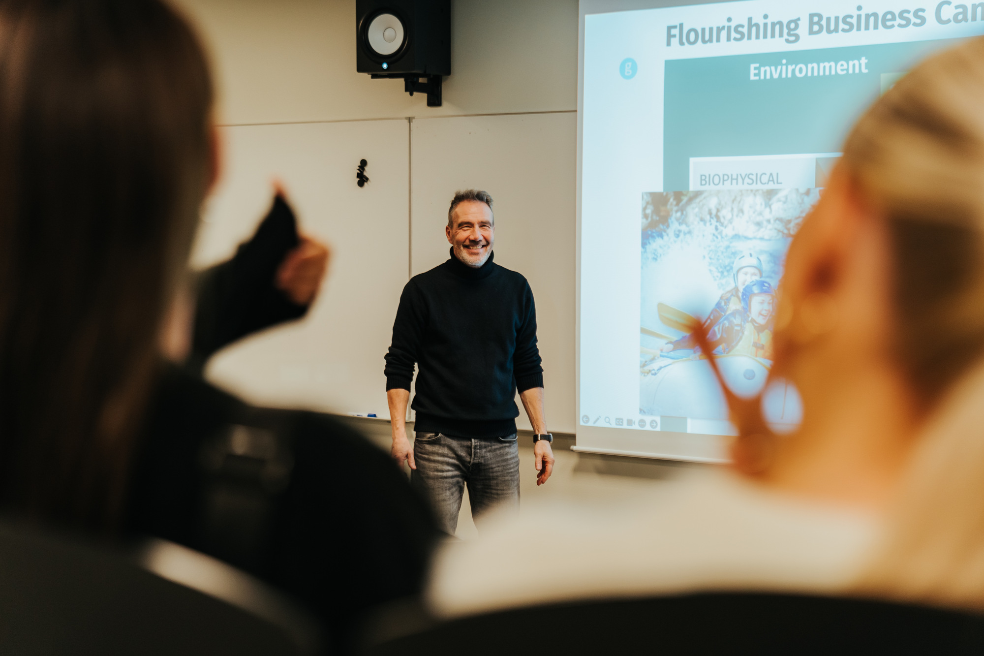 Claus står foran en powerpoint-fremvisning. I forgrunnen ser vi studenter med ryggen til.