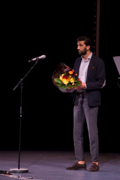 Foto av student på scene med blomster i hånda.