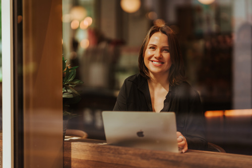 Kvinnelig nettstudent med mac fotografert gjennom et vindu.