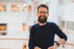 Foto av mann med briller og skjegg i blå genser som lener seg på et rekkverk.