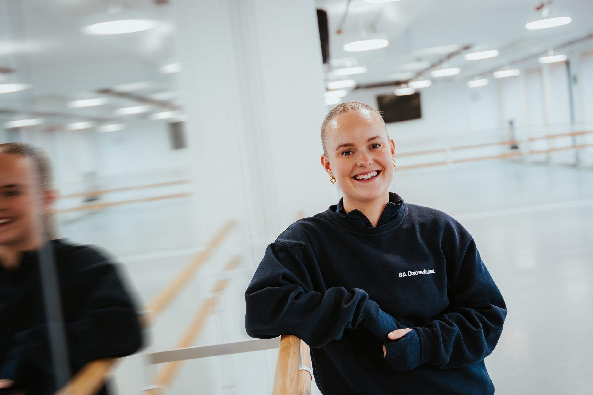 Pauline står i dansestudio ved et speil og smiler til kamera. 