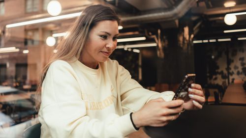 Kvinne sitter ved et bord og ser på telefonen sin. 