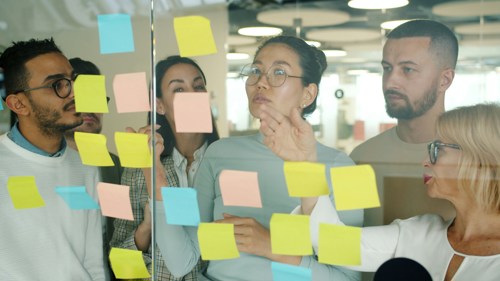 En gruppe kollegaer jobber med post-it lapper på en glass-vegg