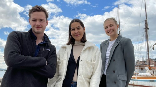 De tre studentene bak Paramate står på en bygge på solfylt dag og smiler inn i kameraet.